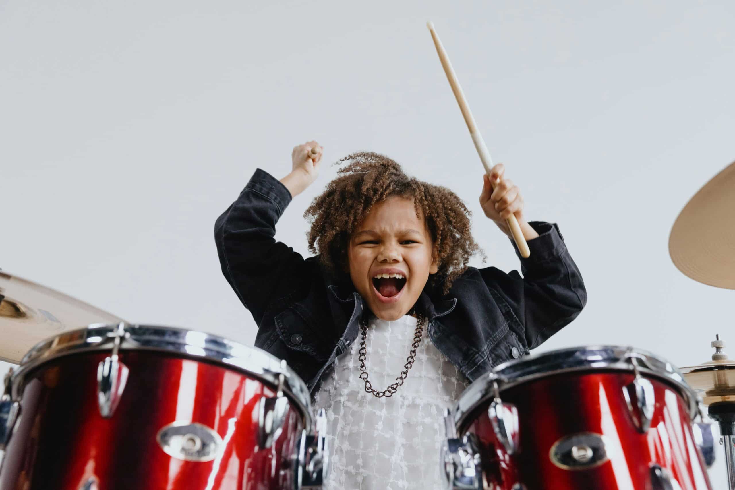 Kid playing drums with a wild expression.