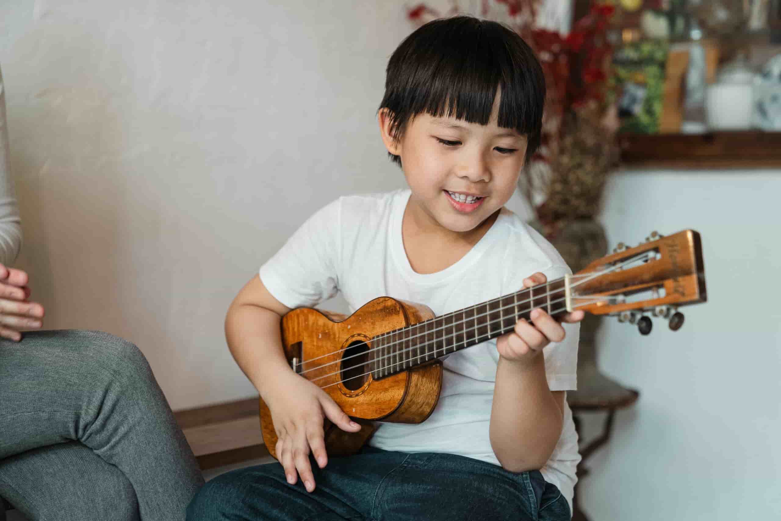 Kid taking ukulele lessons, smiling while playing the ukulele.