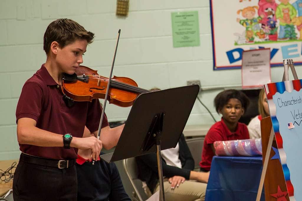 Violin lessons in school, boy playing the violin while another boy looks at him.