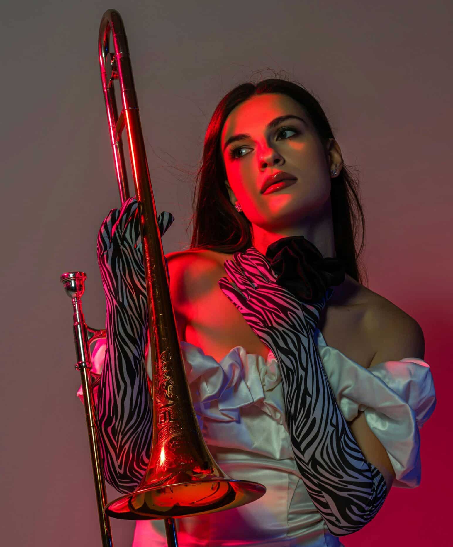 Woman standing holding a trombone upright with a red backdrop