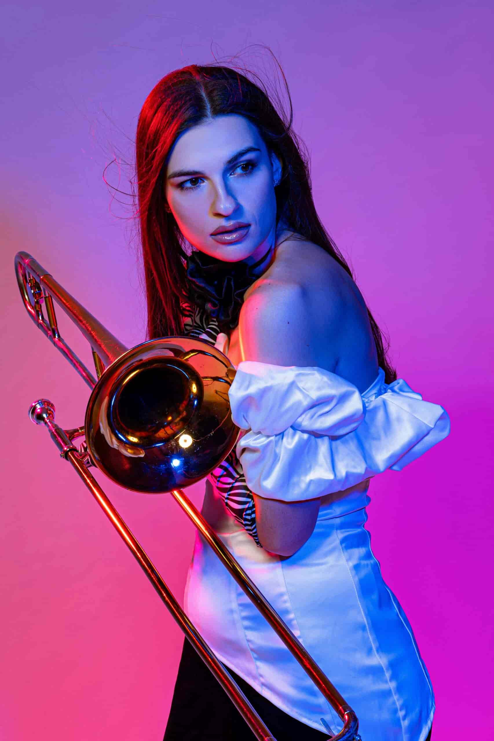 A woman holding a trombone with pink and purple back drop