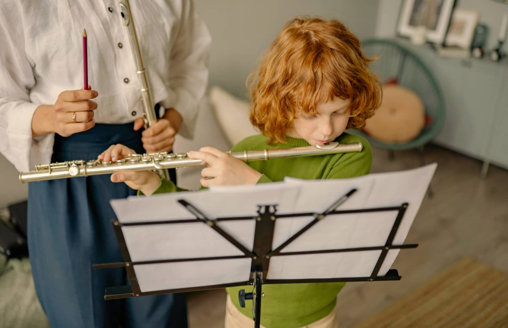 Kid playing flute during flute lessons with teacher on the left