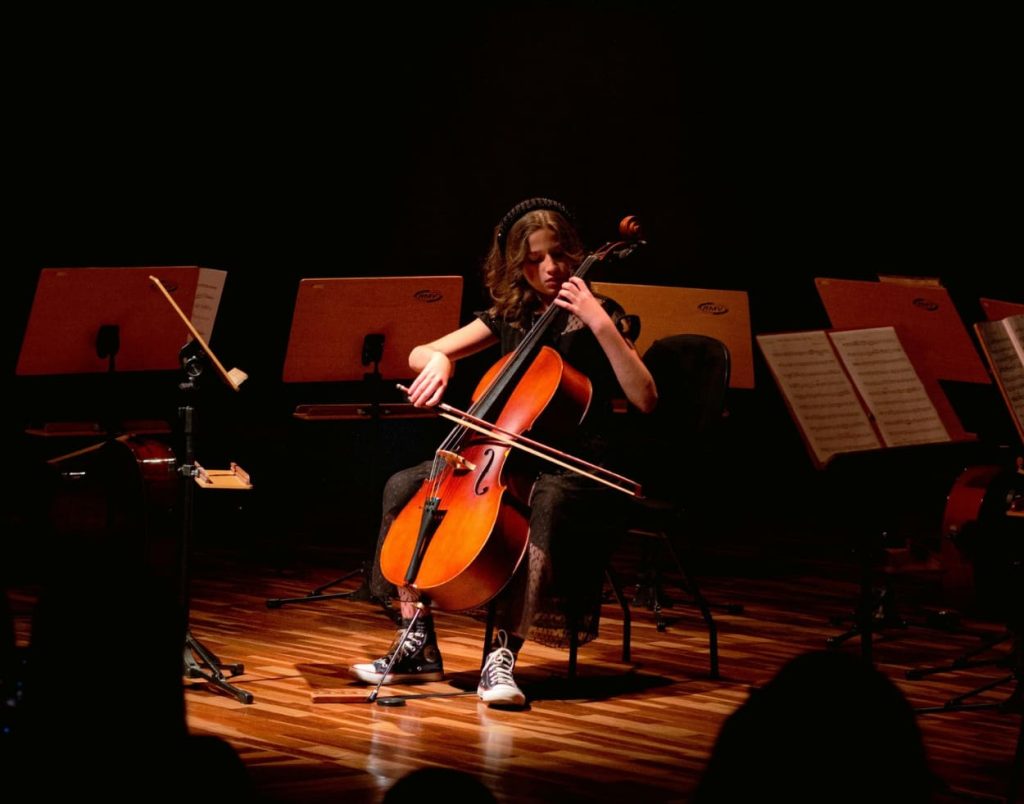 Cello student performing on stage with smaller cello