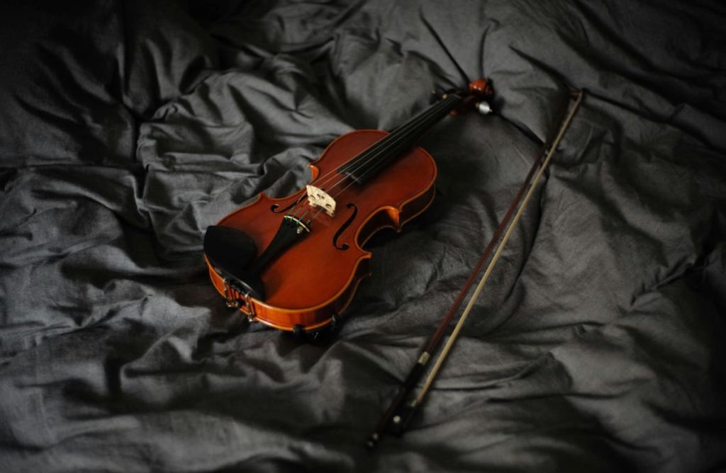 A violin and a bow are placed on a grey soft cloth.