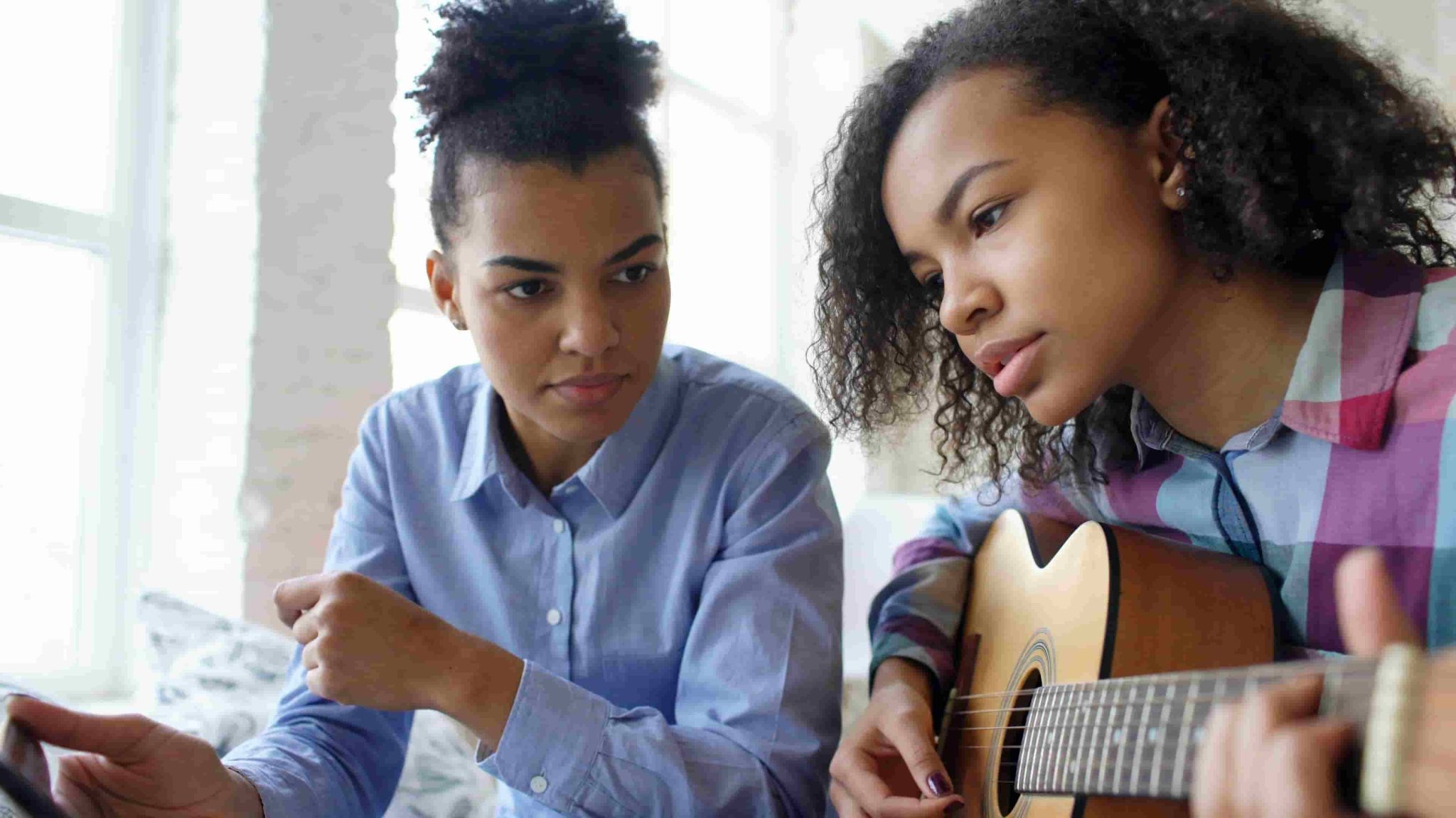 A female music tutor guiding a young student during a private acoustic guitar lesson in a bright Sydney studio.