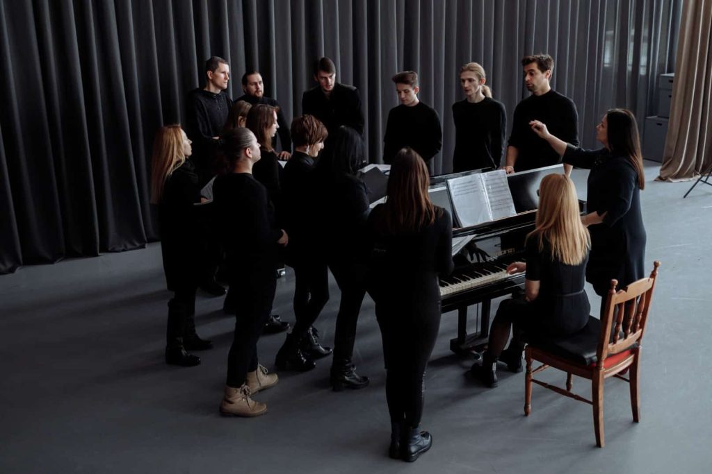 choir with a conductor standing around a piano accompanist