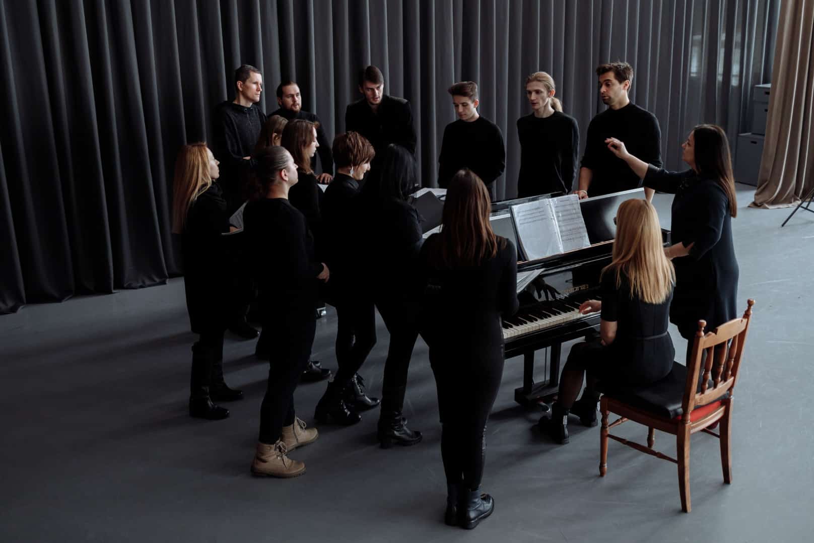 choir with a conductor standing around a piano accompanist