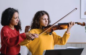 A violin teacher helping a beginner student practice during a violin lesson.