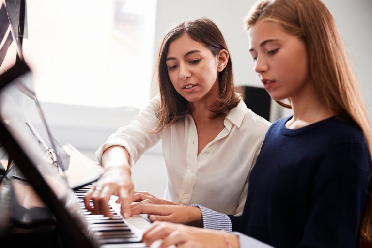 A teacher teaching a girl to play piano